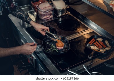 A Man With Tattooed Arm Grilling A Beef In A Kitchen.