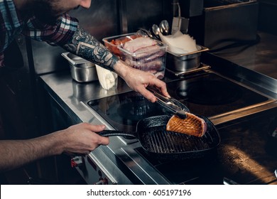 A Man With Tattooed Arm Grilling A Beef In A Kitchen.