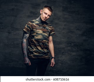 A man with tattoos on his neck, face and arms, dressed in a camouflage t shirt.
