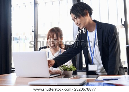 A man teaching a computer in the office and a young woman being taught