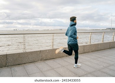 A man in a teal jacket keeps pace along the river walk, under a dramatic sky suggestive of impending weather.