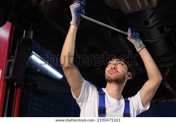 Man technician car mechanic in uniform checking\
or maintenance a lifted car service at repair garage station.\
Worker holding wrench and fixing breakdown vehicle. Concept of car\
center repair service.