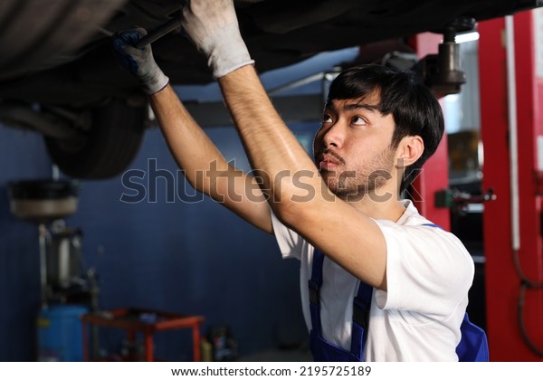 Man technician car mechanic in uniform checking\
or maintenance a lifted car service at repair garage station.\
Worker holding wrench and fixing breakdown vehicle. Concept of car\
center repair service.