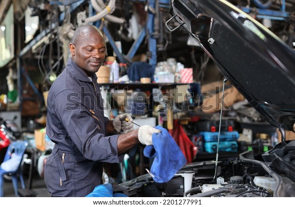 Man\
technician car mechanic in uniform checking maintenance a car\
service at repair garage station. Worker checking motor oil level\
in car engine. Concept of car center repair\
service.