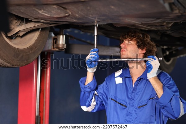 Man technician car mechanic in uniform checking\
or maintenance a lifted car service at repair garage station.\
Worker holding wrench and fixing brake discs. Concept of car center\
repair service.