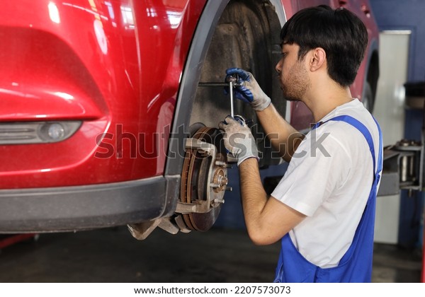 Man technician car mechanic in uniform checking\
or maintenance a lifted car service at repair garage station.\
Worker holding wrench and fixing brake discs. Concept of car center\
repair service.