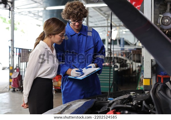 Man technician car mechanical in\
uniform showing car maintenance service report on clipboard at\
repair garage station. Auto mechanic give customer discussion on\
her vehicle repairs\
problems condition