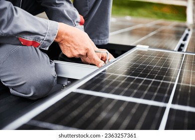 Man technician mounting photovoltaic solar panels on roof of house. Close up view of mounter installing solar module system with help of hex key. Concept of alternative, renewable energy.
