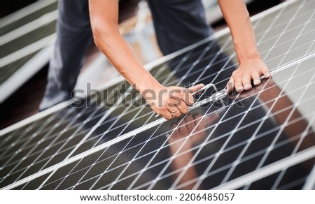 Man technician mounting photovoltaic solar moduls on roof of house. Close up of electrician installing solar panel system with help of hex key. Concept of alternative and renewable energy.