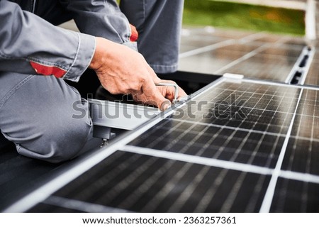 Man technician mounting photovoltaic solar panels on roof of house. Close up view of mounter installing solar module system with help of hex key. Concept of alternative, renewable energy.