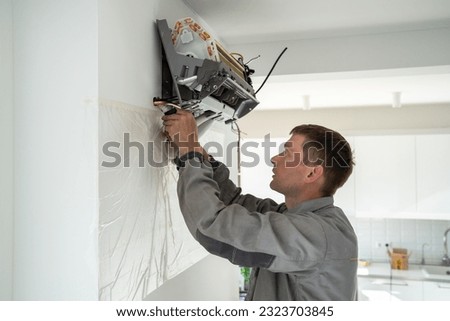 Man technician worker in uniform fixing repairing apartment air conditioner, installing wall-mounted mini split. AC unit maintenance concept