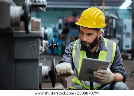 Man technician worker using tablet control setting up checking operating machinery of lathe metal factory industrial. Male worker wear yellow hardhat controlling at industrial workshop.