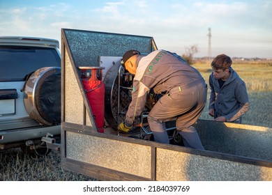 A Man And A Teenager Are Loading And Unloading Equipment From A Car Trailer For Further Work