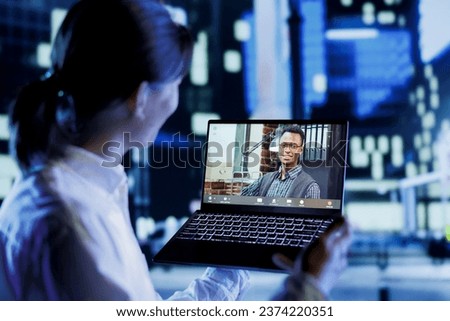 Man in teleconference meeting with coworker while strolling around city streets at night, giving him work updates. Citizen using laptop to show colleague nighttime metropolitan environment