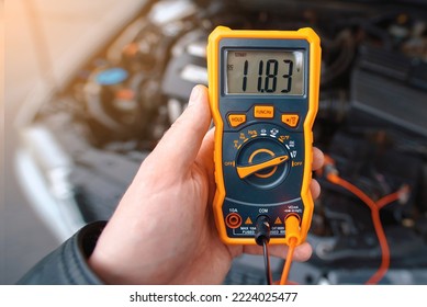 Man testing car electrical system including battery, alternator for winter. Check car battery using voltmeter. Man use multimeter with voltage range measurement to check up voltage level. Low voltage