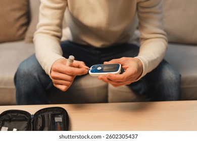 Man testing glucose level with glucometer at home selective focus on hands. Health care concept