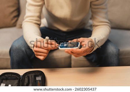 Man testing glucose level with glucometer at home selective focus on hands. Health care concept
