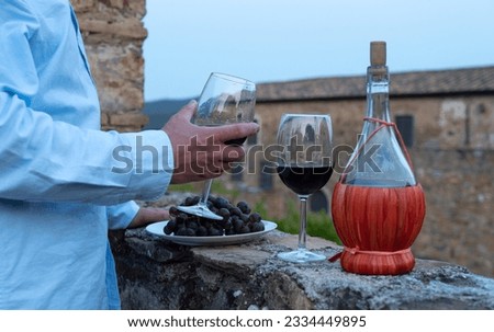 Man testing red wine from the typical chianti wine bottle fiasco against the backdrop of the Tuscany landscape