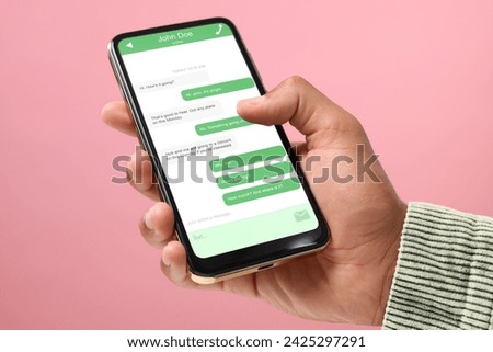 Man texting with friend using messaging application on smartphone against pink background, closeup