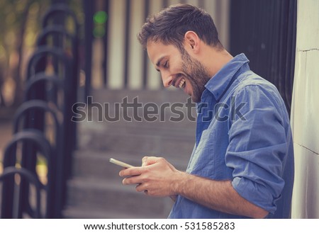 Man texting on phone. Casual urban professional entrepreneur using smartphone smiling happy outside office building. Outdoor portrait of modern young guy with mobile in the street
