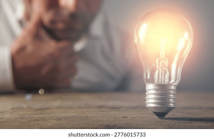 Man thinking and looking at a light bulb on a wooden table.