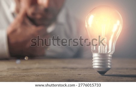 Man thinking and looking at a light bulb on a wooden table.