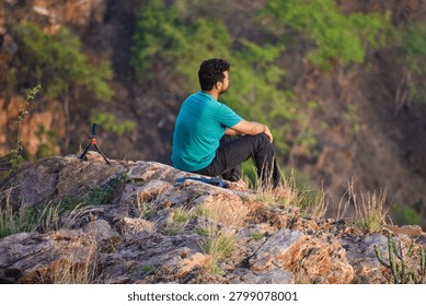 Man thinking while sitting on cliff of mountain 