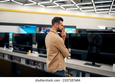 Man Thoughtfully Put His Hand To His Chin And Chooses New Plasma TV In Store Of Household Appliances, Gadgets And Electronics. Buying New Plasma.