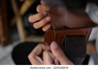 a man with threads and needle , making leather goods with handstitched process
