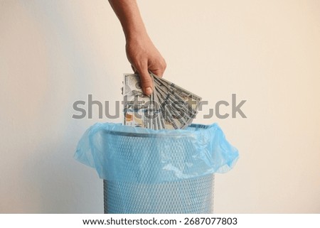 Man throwing dollar banknotes into trash bin on white background, closeup