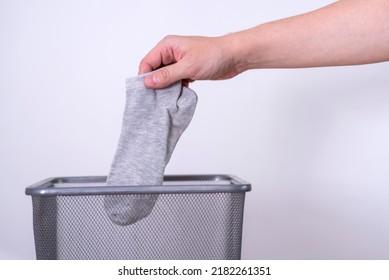 Man Throwing An Old Sock With His Hand Into A Trash Can Against A Gray Background. The Concept Of Old Clothes.