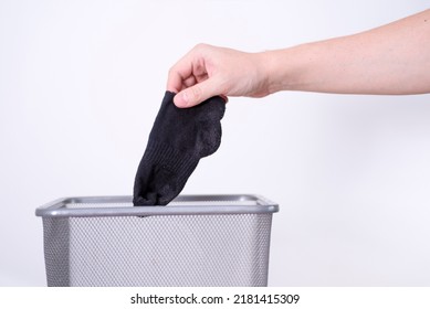 A Man Is Throwing An Old Sock Into A Trash Can With His Hand Against A White Background. The Concept Of Old Clothes.