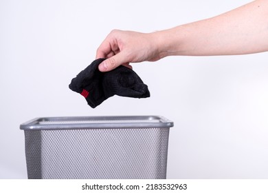 A Man Is Throwing An Old Sock Into A Trash Can With His Hand Against A White Background. The Concept Of Old Clothes.