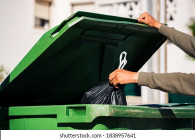 Man throwing out black eco-friendly recyclable trash bag in to big plastic green garbage container. Take out the trash - Shutterstock ID 1838957641