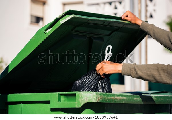 Man\
throwing out black eco-friendly recyclable trash bag in to big\
plastic green garbage container. Take out the\
trash