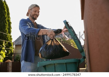 Man throwing trash bag full of garbage into bin outdoors