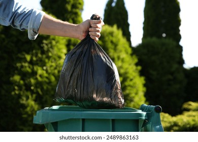 Man throwing trash bag into bin outdoors, closeup