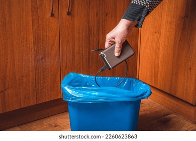 A man throws an external hard drive into the trash can. Man's hand with an external drive and a trash can in blue.