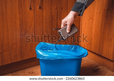 A man throws an external hard drive into the trash can. Man's hand with an external drive and a trash can in blue.