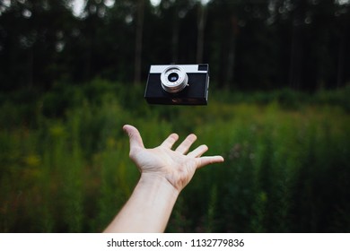 Man throws up the old camera in front of grass and forest