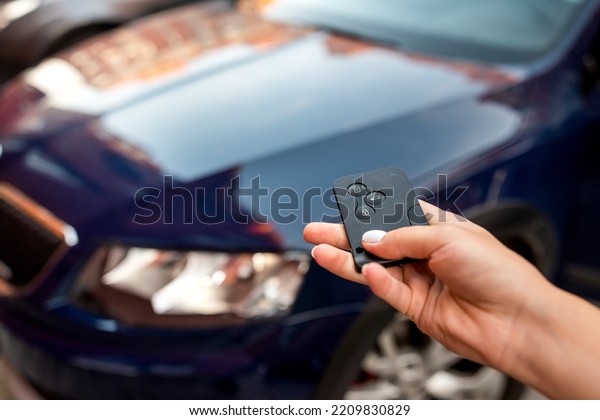 Man with thumb presses\
black button on remote control key removing alarm signal from\
bright car alarm light. Hand with car keys. Opening the car with\
keys in hand