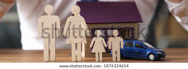 Man in tie holds his hands over wooden\
men with toy house and car closeup. Social guarantees for large\
families home and car insurance\
concept.