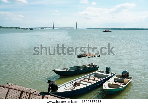 A man\
tie a rope to secure his boat to a wooden jetty with johor bridge\
in the background. view from a wooden\
jetty