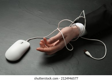 Man tied with computer mouse cable at black table, closeup. Internet addiction