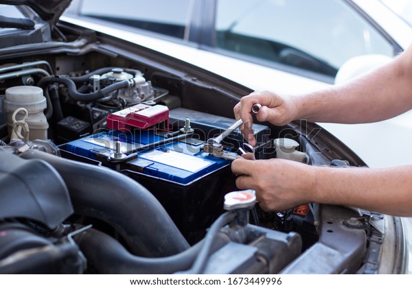 a man tightens with a\
wrench bolts for fastening a new battery, installing spare parts\
for a car