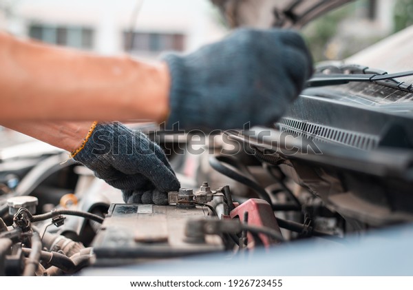 a man tightens with a\
wrench bolts for fastening a new battery, installing spare parts\
for a car