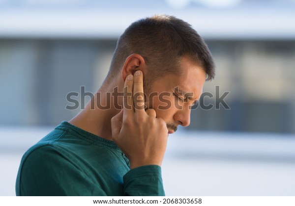 Man with tinnitus. Man touching his ear\
because of strong earache or ear pain.\
Otitis