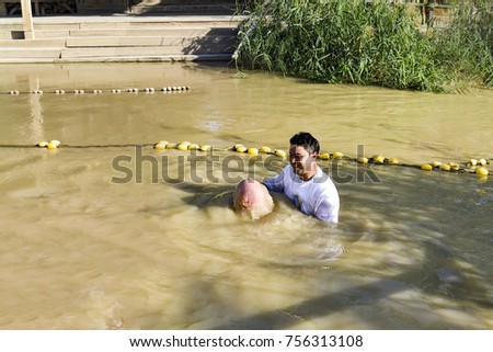 a man toes underwater at his baptism in the Jordan River. The priest holds his hands