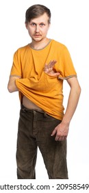 A Man In A Torn Orange T-shirt And Old Corduroy Brown Trousers Stuck His Hand Into The Hole In The T-shirt And Looks At Us In Surprise. Isolated, White Background