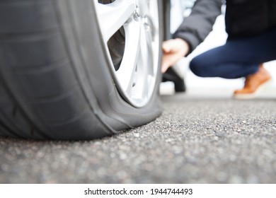 man touching a flat tire on the roadside - Shutterstock ID 1944744493